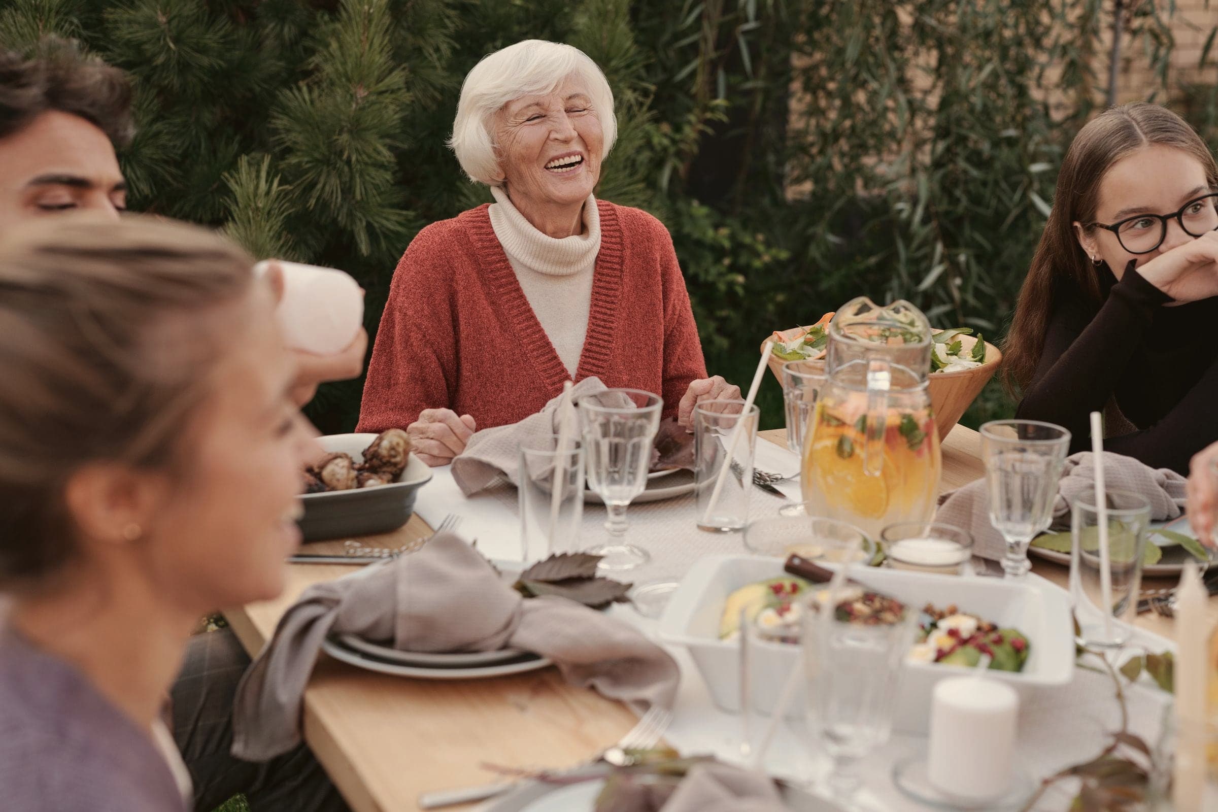 Une grand-mère rit avec ses proches autour d’un déjeuner dans le jardin.