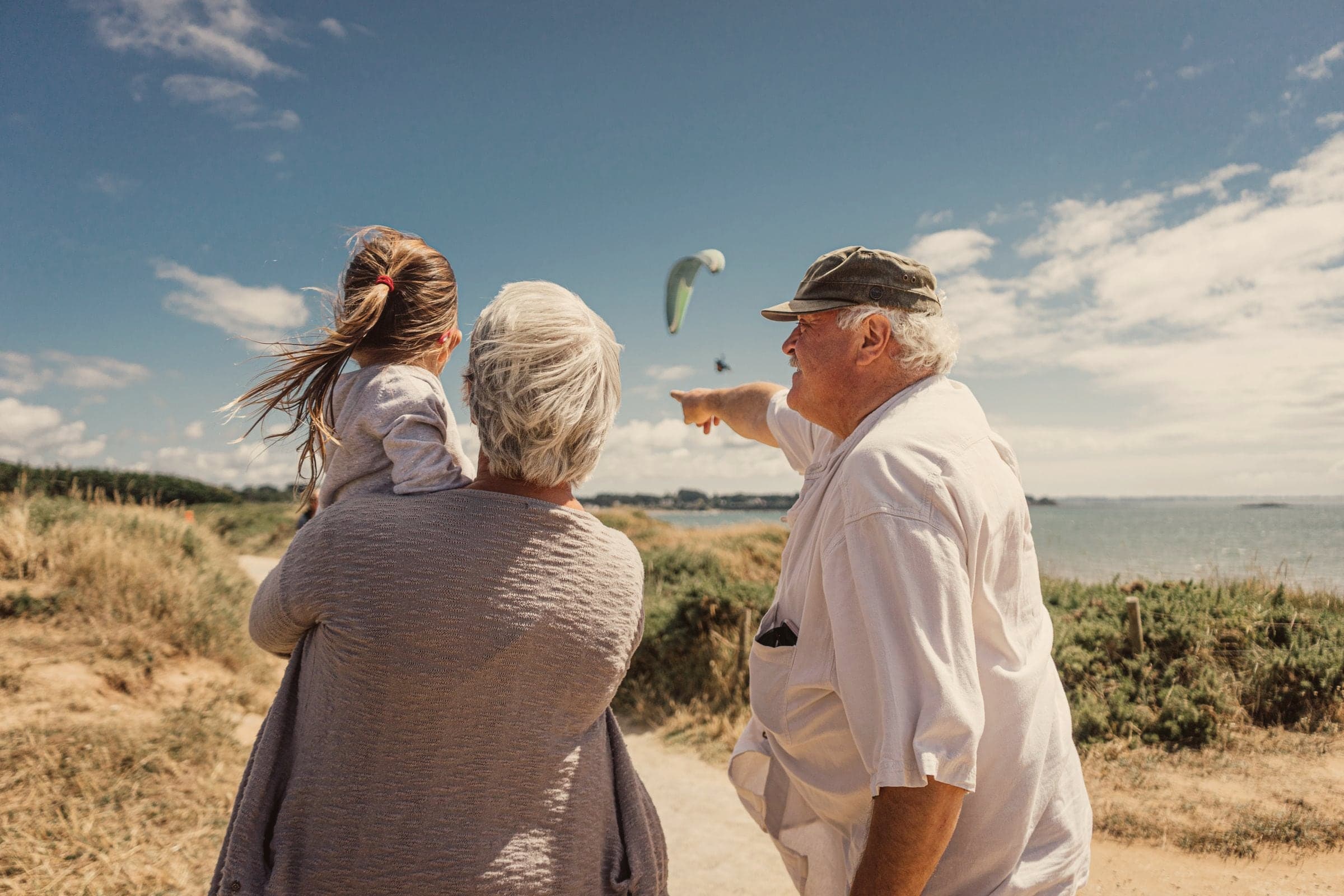Des grands-parents et leur petite-fille regardent la mer depuis un sentier de la côte bretonne, un jour d’été.