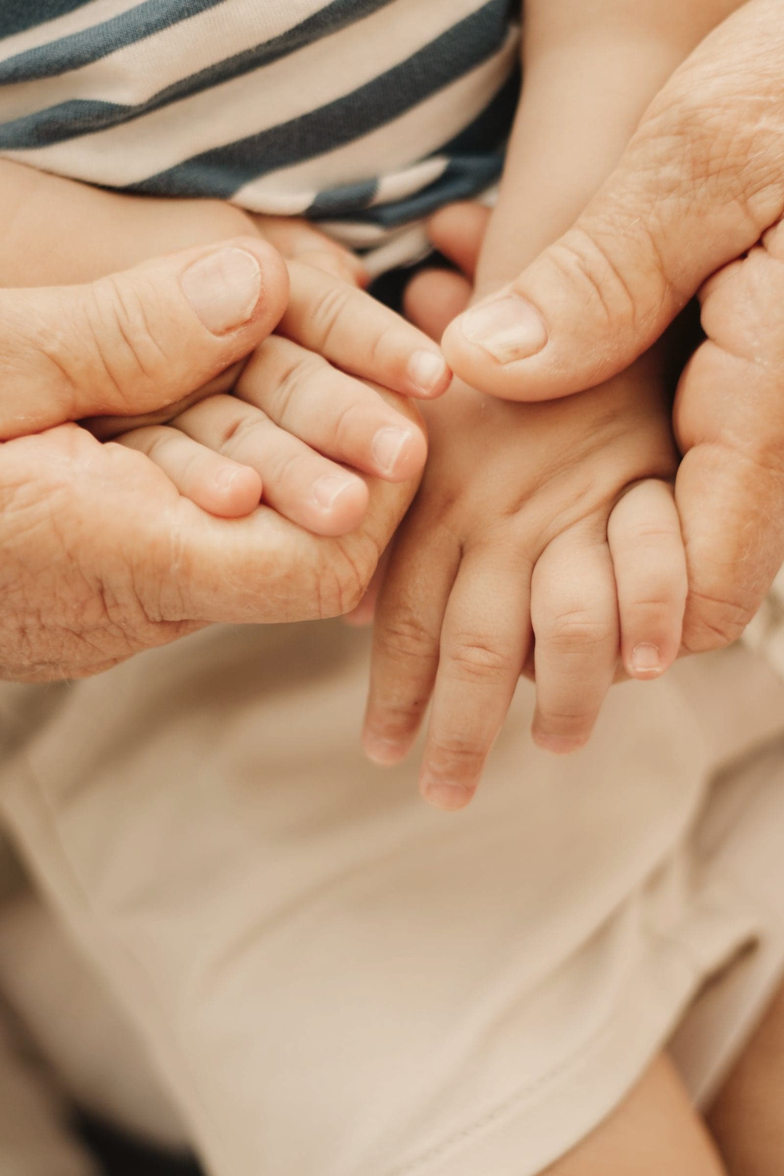 Les mains d’une grand-mère qui tiennent celles d’un jeune enfant.