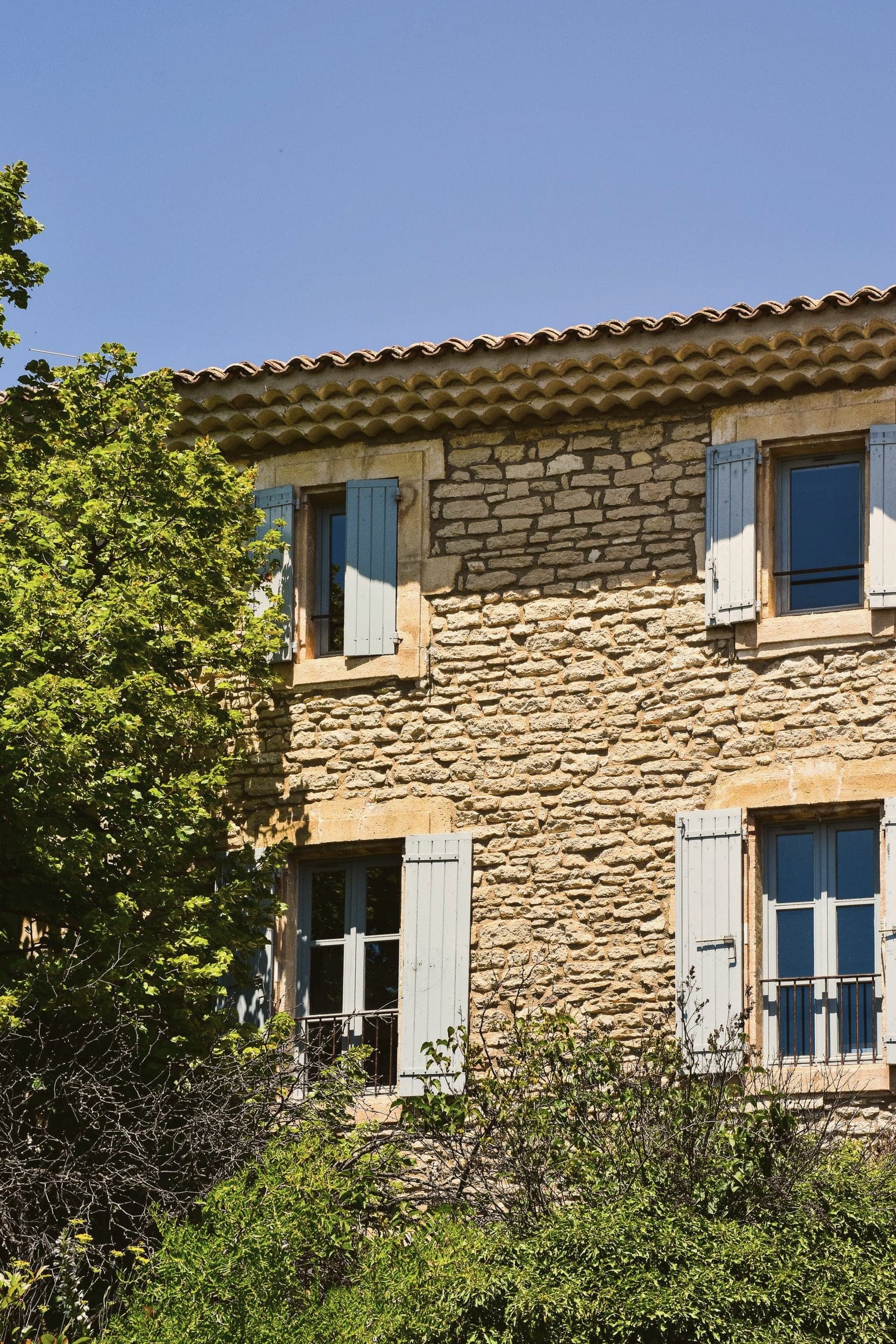 Une maison de pierre provençale aux volets bleus, au soleil d’été.